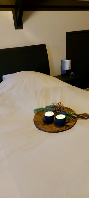 Zwart bed met wit beddengoed houten snijplank met koffiekopjes en kerstgroen