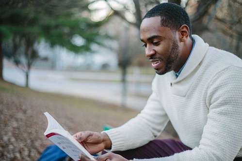 young man in a white sweater sitting and reading a book