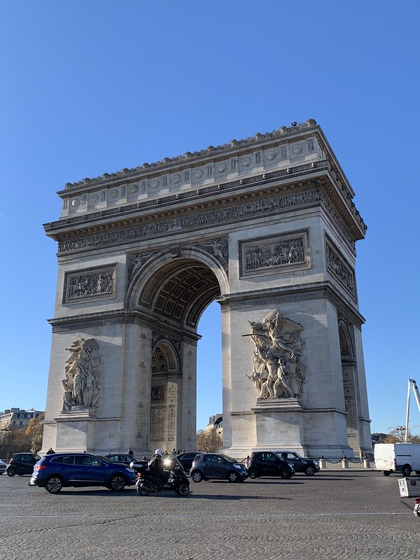 A street view of the arched monument in front of a blue sky.