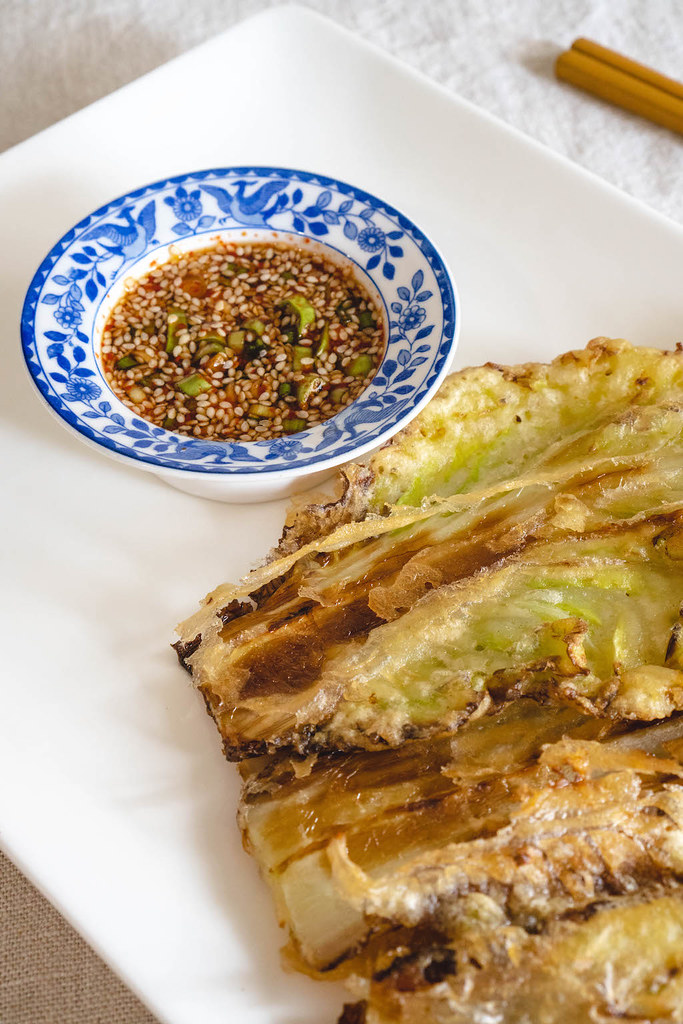 An overhead shot of dipping sauce in a blue and white bowl next to baechu jeon. 