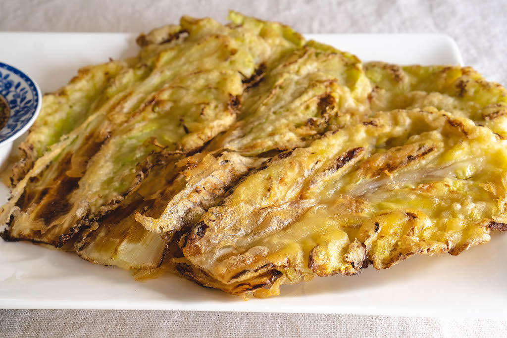 A side shot a Korean cabbage pancakes on a white plate. 