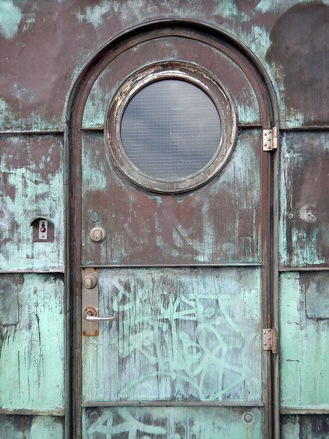 copper door with a verdigris patina with a porthole window on a bridge tower in Copenhagen, Denmark