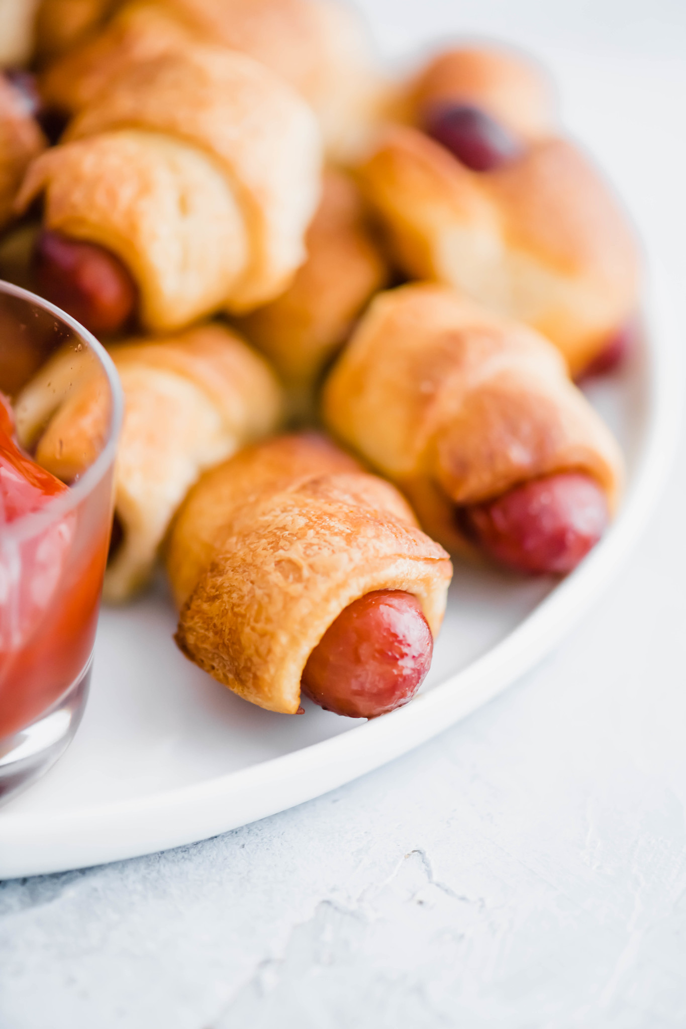 Close up of a few pigs in a blanket on a white round plate.