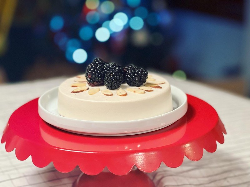 Christmas Eve 2021 vegan cheesecake topped with blackberries and sliced almonds displayed on a red metal cake stand
