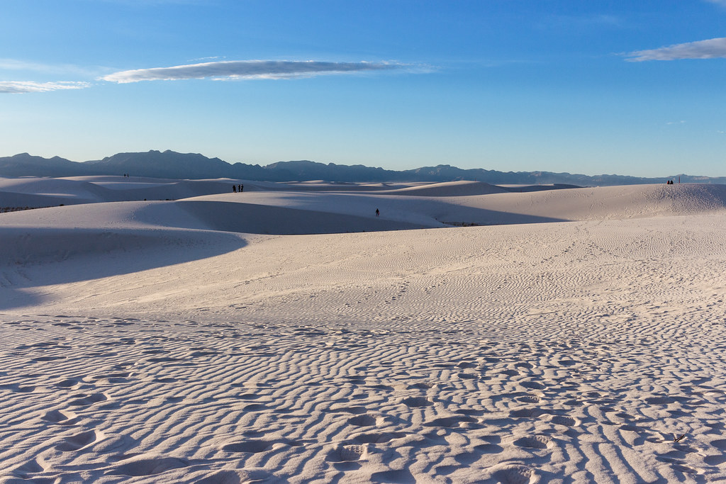 Footprints cover the many furrows in white sand dunes caused by wind on a late afternoon