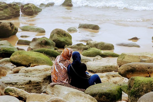 Two women perched on rocks by the sea, listening to each other. From Through the Eyes of an Educator: Cultivating Compassion, Kindness, & Empathy