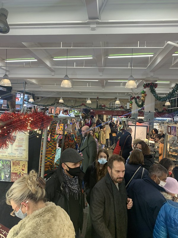 People crowd the aisles of a Christmas market where different products and and stands fill the indoor space.