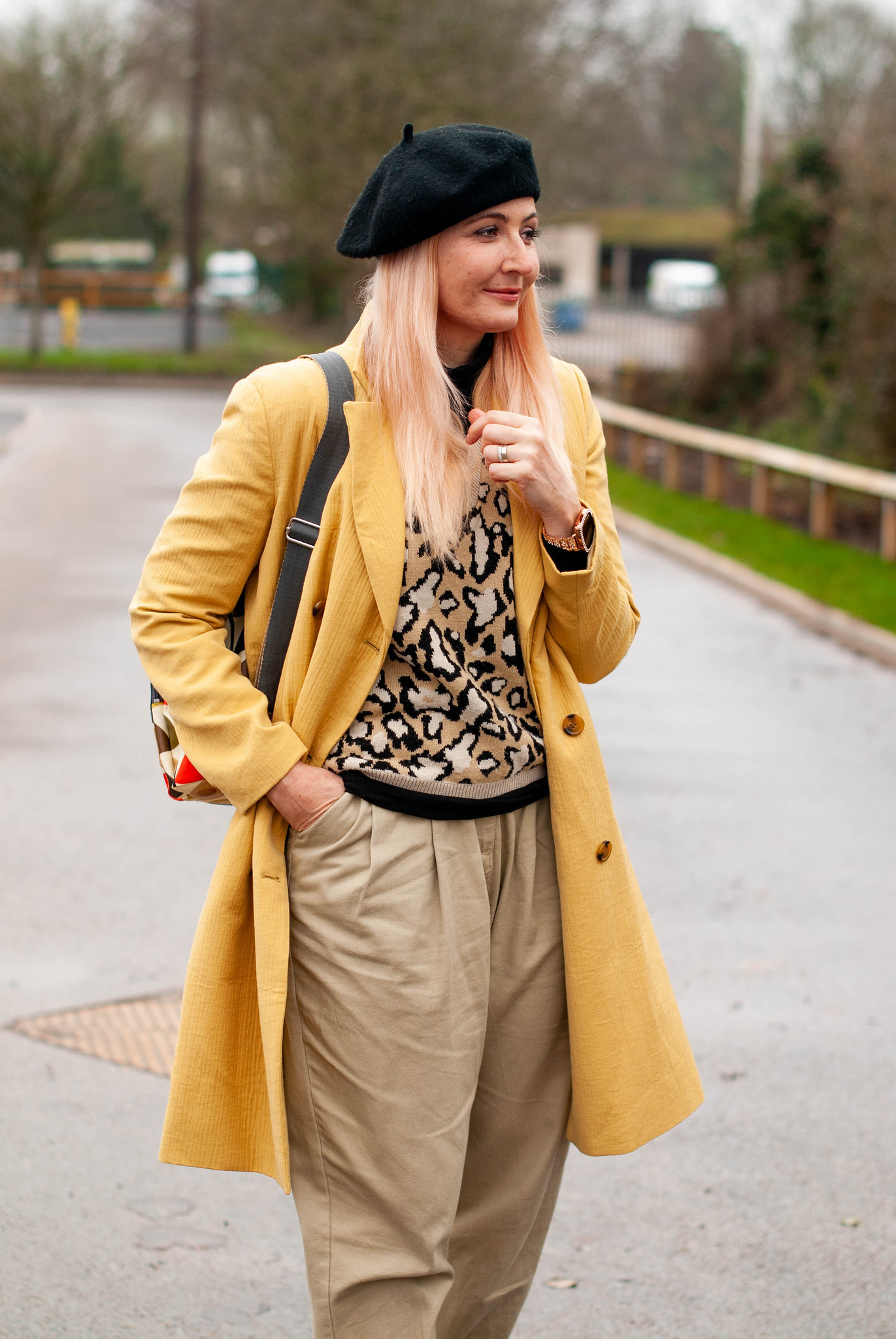 Casual French-inspired winter chic: Catherine Summers of Not Dressed As Lamb wearing a yellow longline coat, leopard knit tank top, stone baggy trousers, black flatforms, black beret, Orla Kiely stems backpack | Fashion Over 40