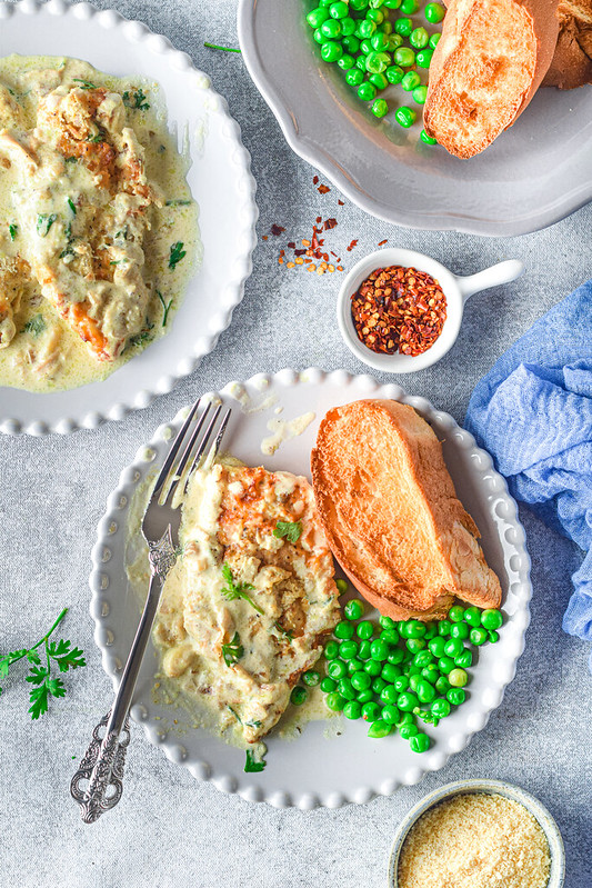 Overhead shot of creamy parmesan chicken on a plate with peas and toasted bread