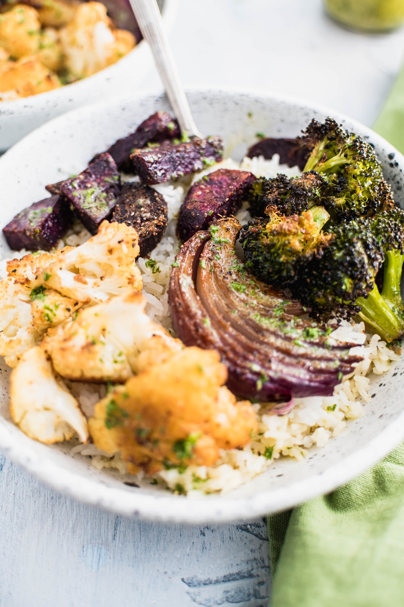 Close up photo of white rice topped with roasted cauliflower, broccoli, red onino and purple sweet potatoes.