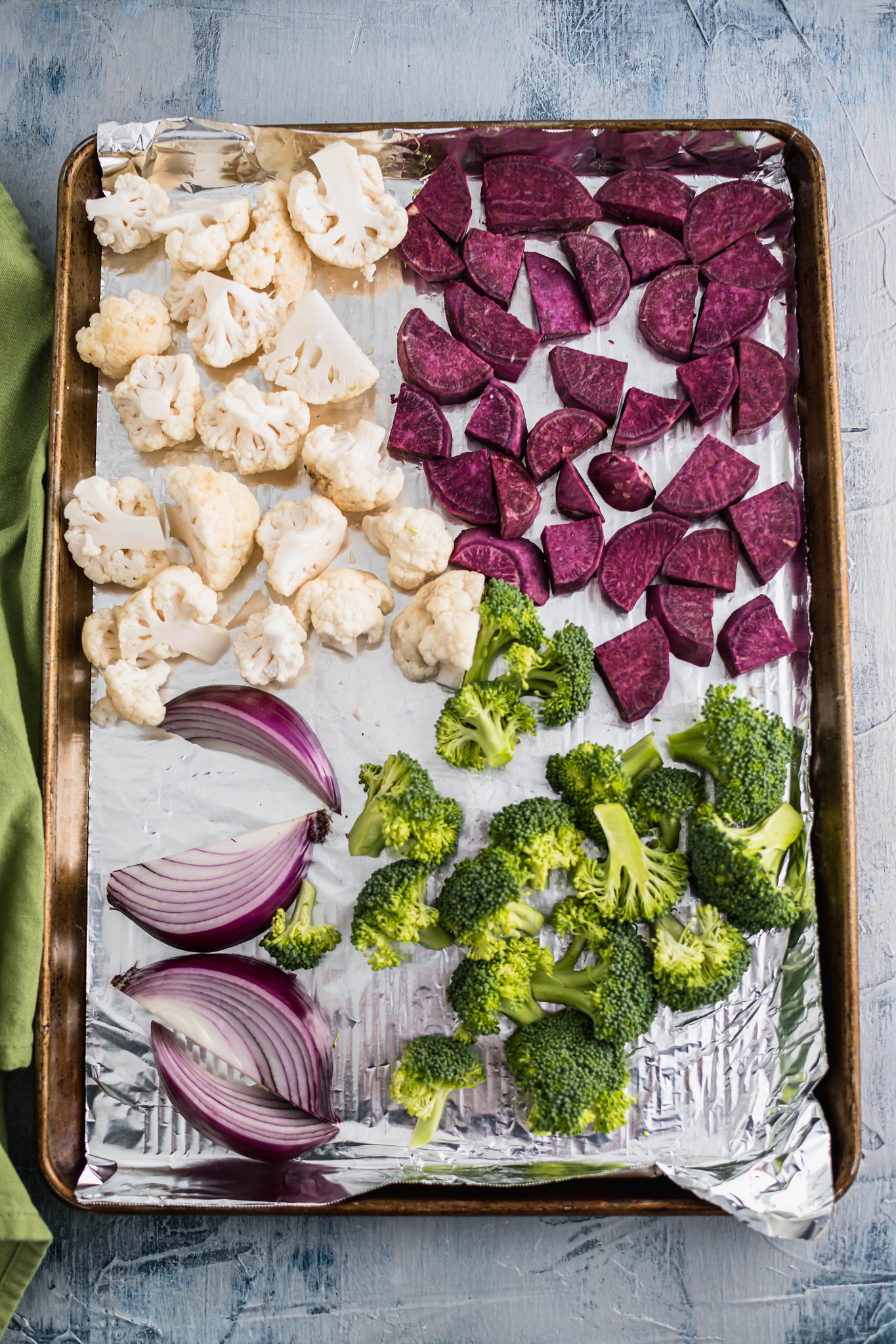Broccoli, caulilower, chopped purple sweet potatoes and red onion on a foil lined baking sheet.