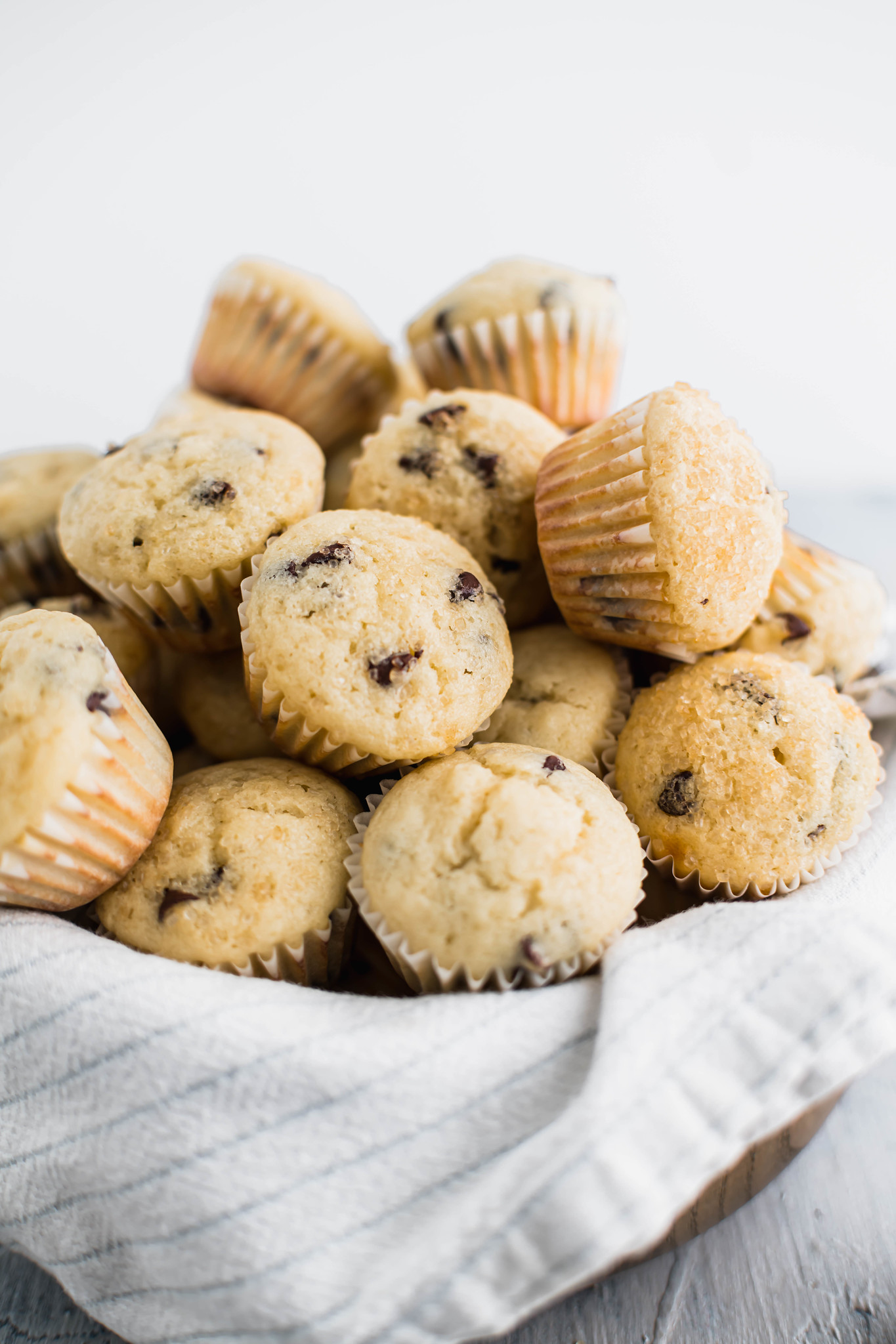Mini chocolate chip muffins piled in a bowl lined with a white and gray striped kitchen towel.