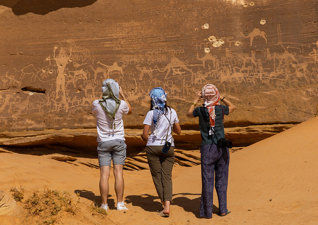 Tourists taking pictures of petroglyphs depicting camels and humans, Najran Province, Thar, Saudi Arabia