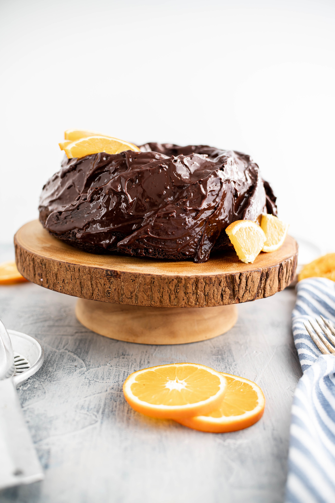 Photo of orange chocolate cake on a wooden cake stand surrounded by slices of oranges.