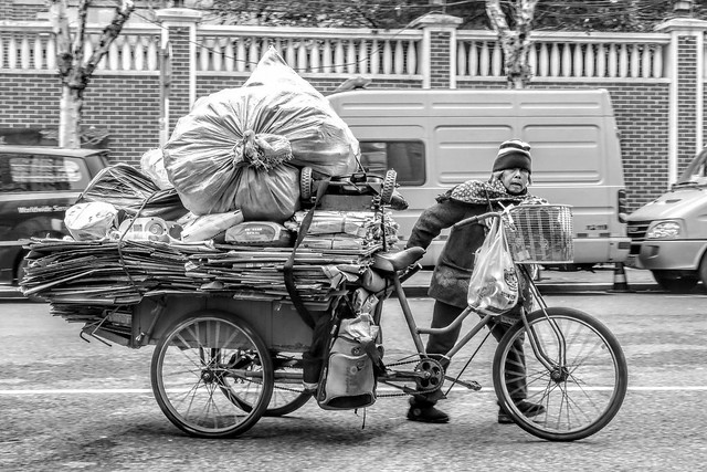 An old woman collecting recyclables struggles to push her tricycle