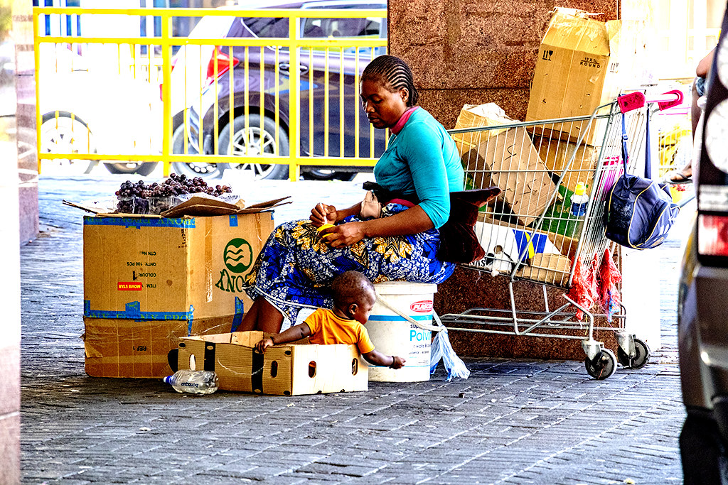 Woman spoon feeding baby while selling on sidewalk on 1-27-22--Windhoek copy