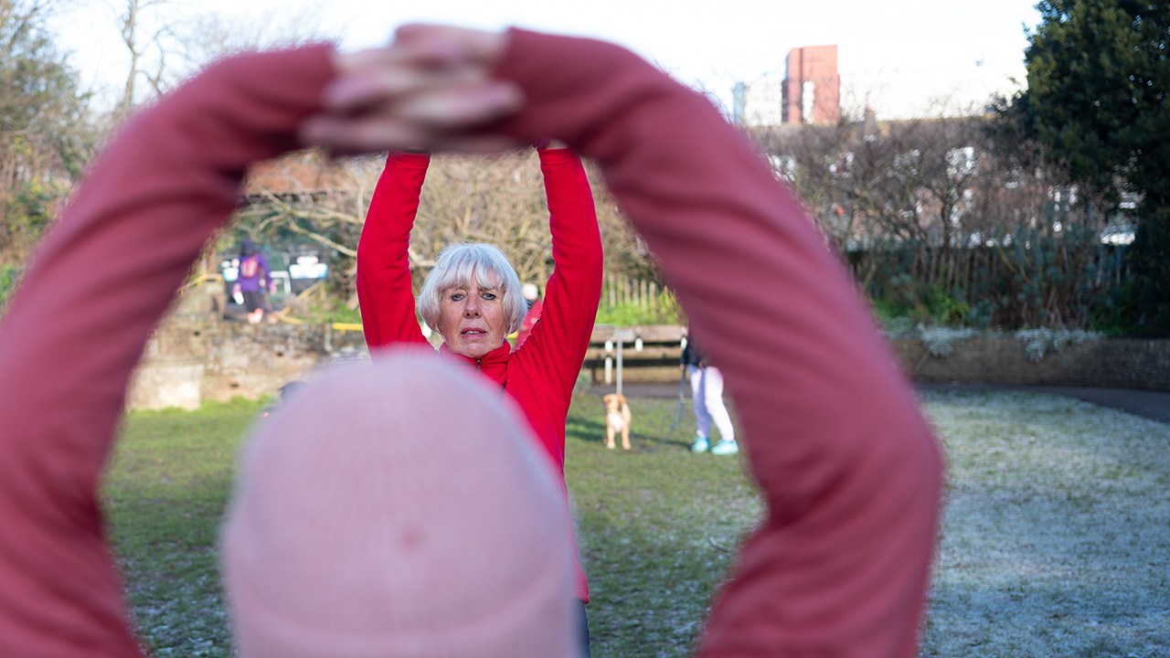 Two older women in sportswear exercising in a park.