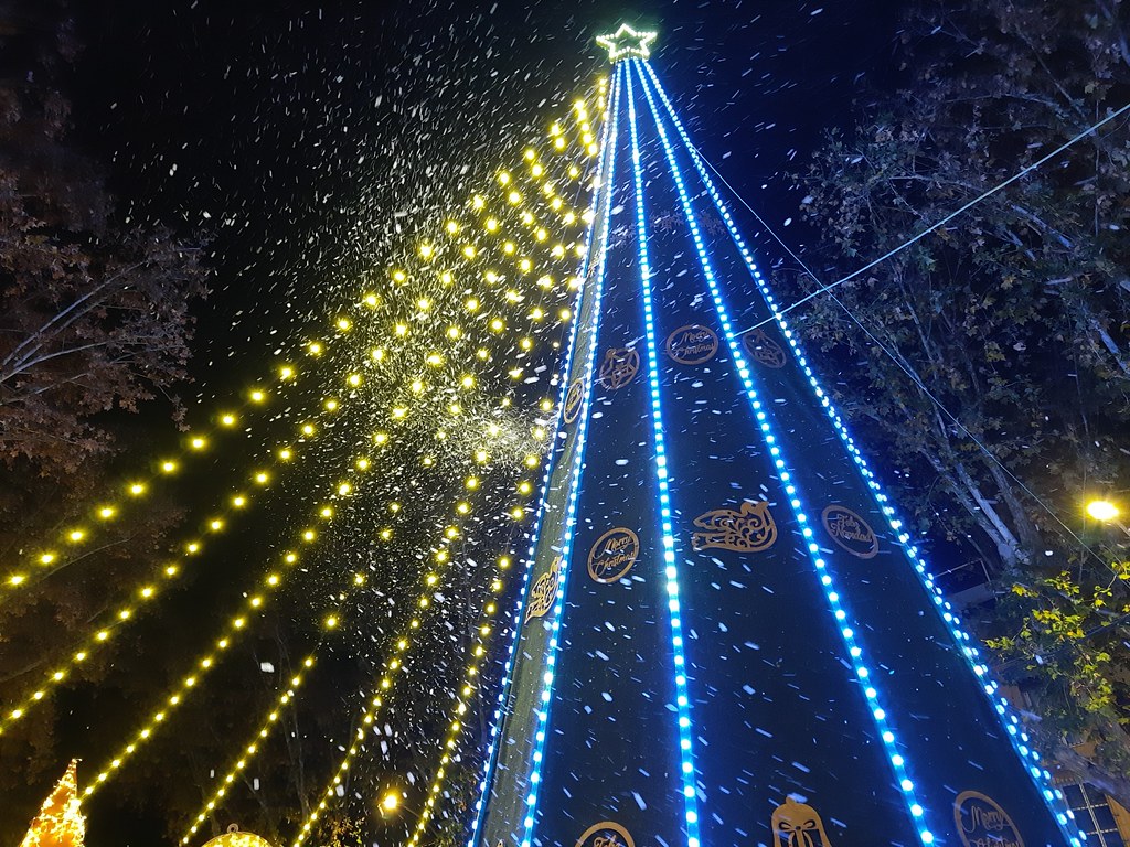 A structure in the shape of a Christmas tree covered with blue and yellow lights. The 