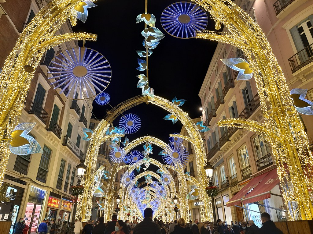 The tunnel of lights from Calle Larios. On each side of the road there are large yellow lights columns that connect to each other on top. Hanging from them there are giant blue circles and stylised wings