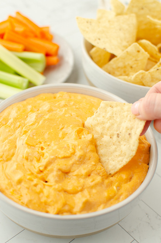 A tortilla chip being dipped in a bowl of buffalo chicken dip. 