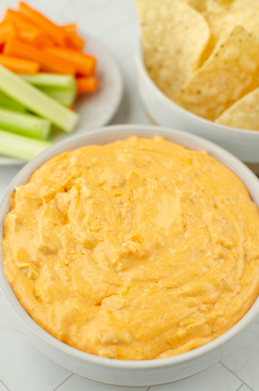 Bowl of buffalo chicken dip with celery, carrots, and tortilla chips