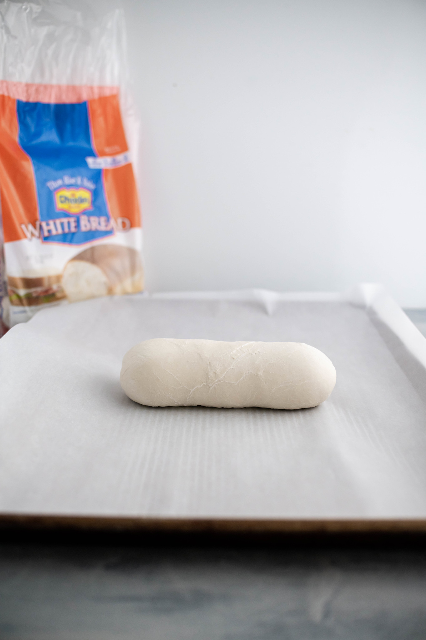 One loaf of Rhodes bread dough on a parchment lined baking sheet.