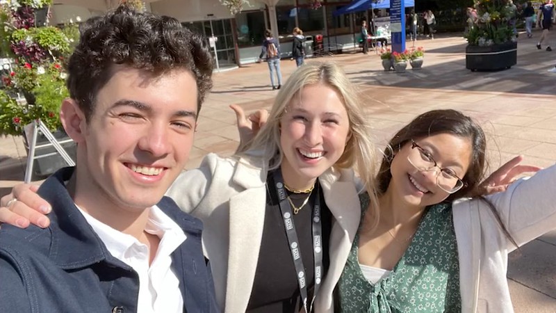 Students Cedric, Anabel and Ammira taking a selfie photo on the Parade at the University of Bath campus.