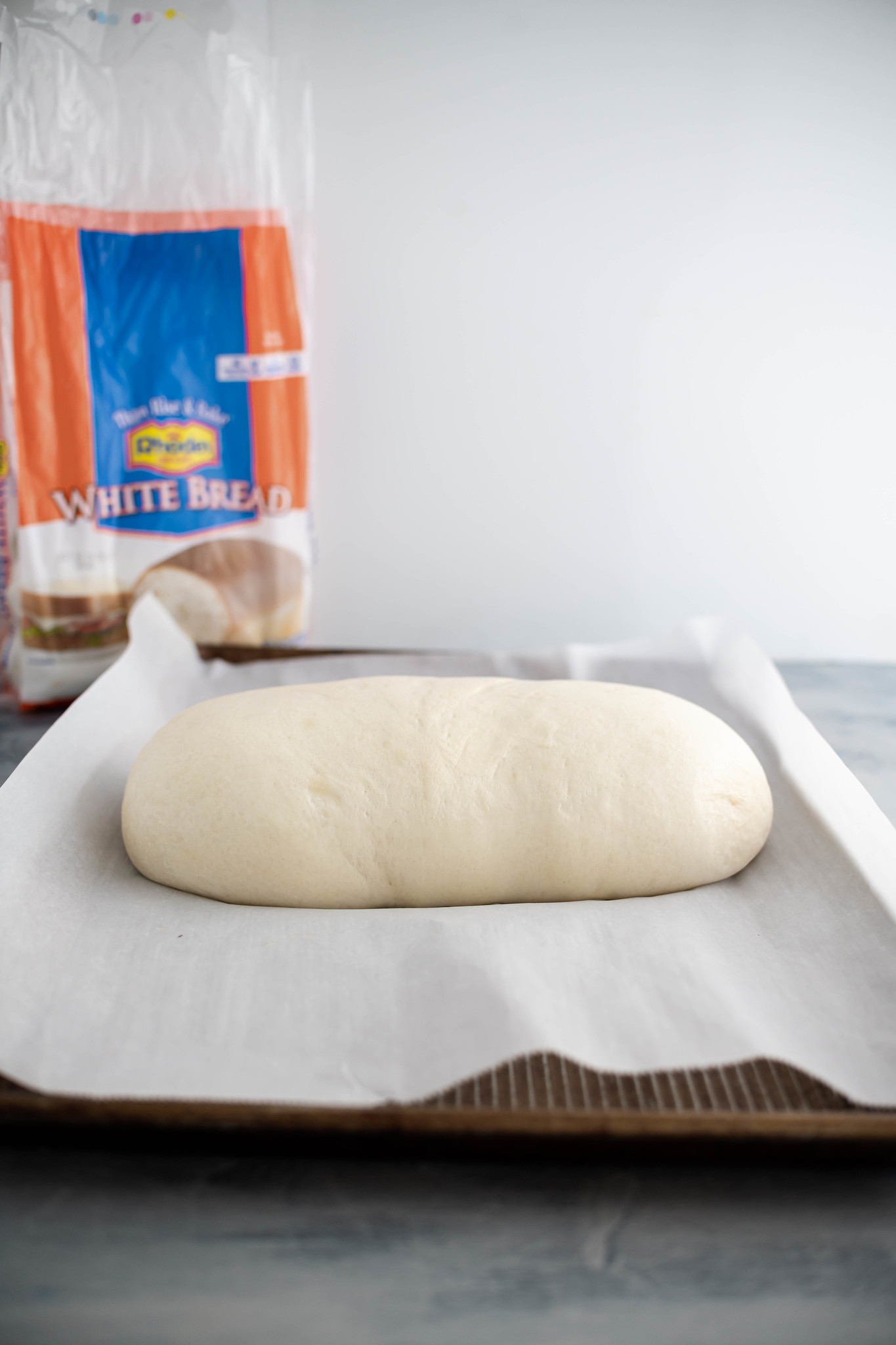 One risen loaf of Rhodes bread dough on a parchment lined baking sheet.