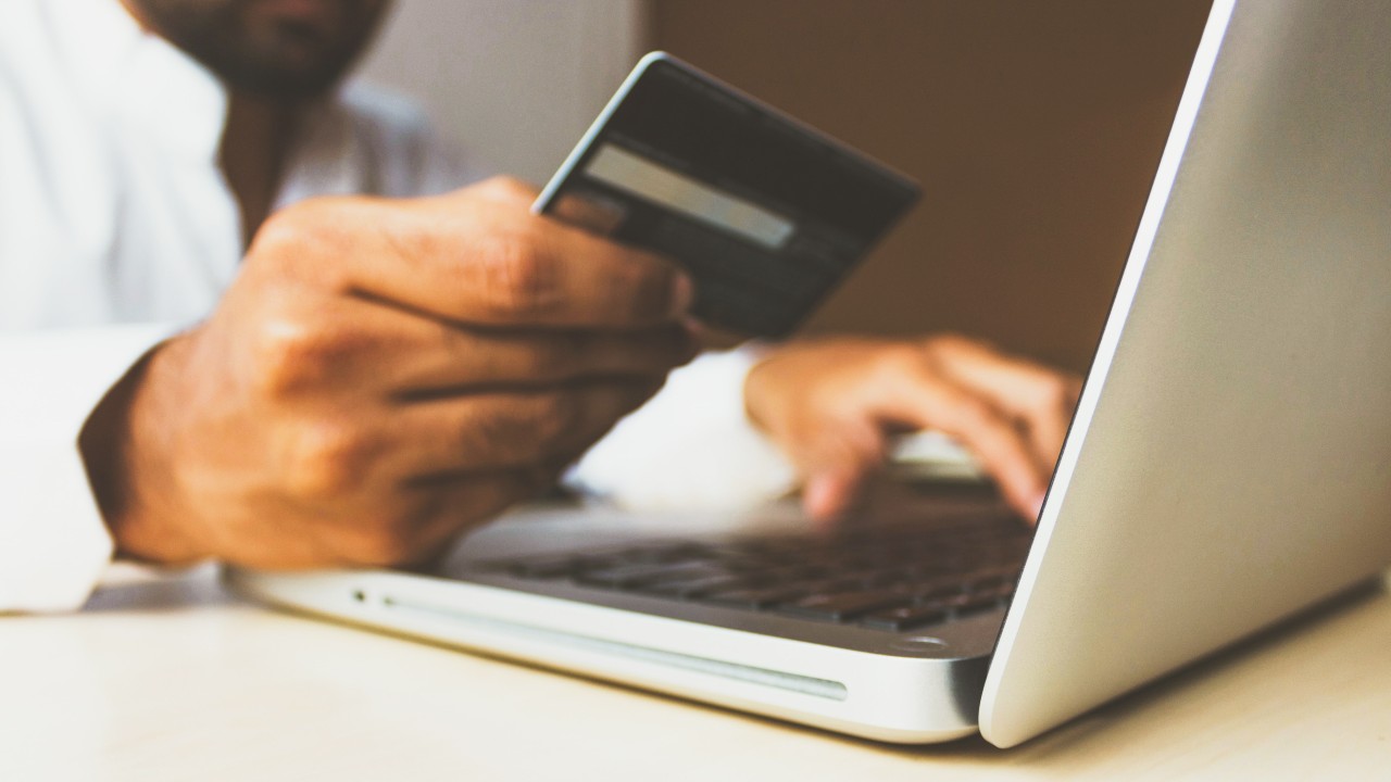 A man looks at his credit card, ready to pay for something at his laptop