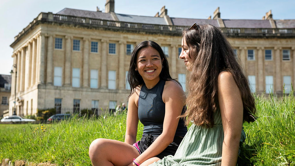 Two students sat on the grass in front of the Royal Crescent