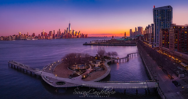 NYC NJ SkylinesNYC NJ Skylines - Aerial view during sunset of Pier C, the iconic Lackawana Train station and the Hoboken, NJ and lower Manhattan New York City skyline. Along the many skyscrapers in the Financial District and Battery Park One World Trade C