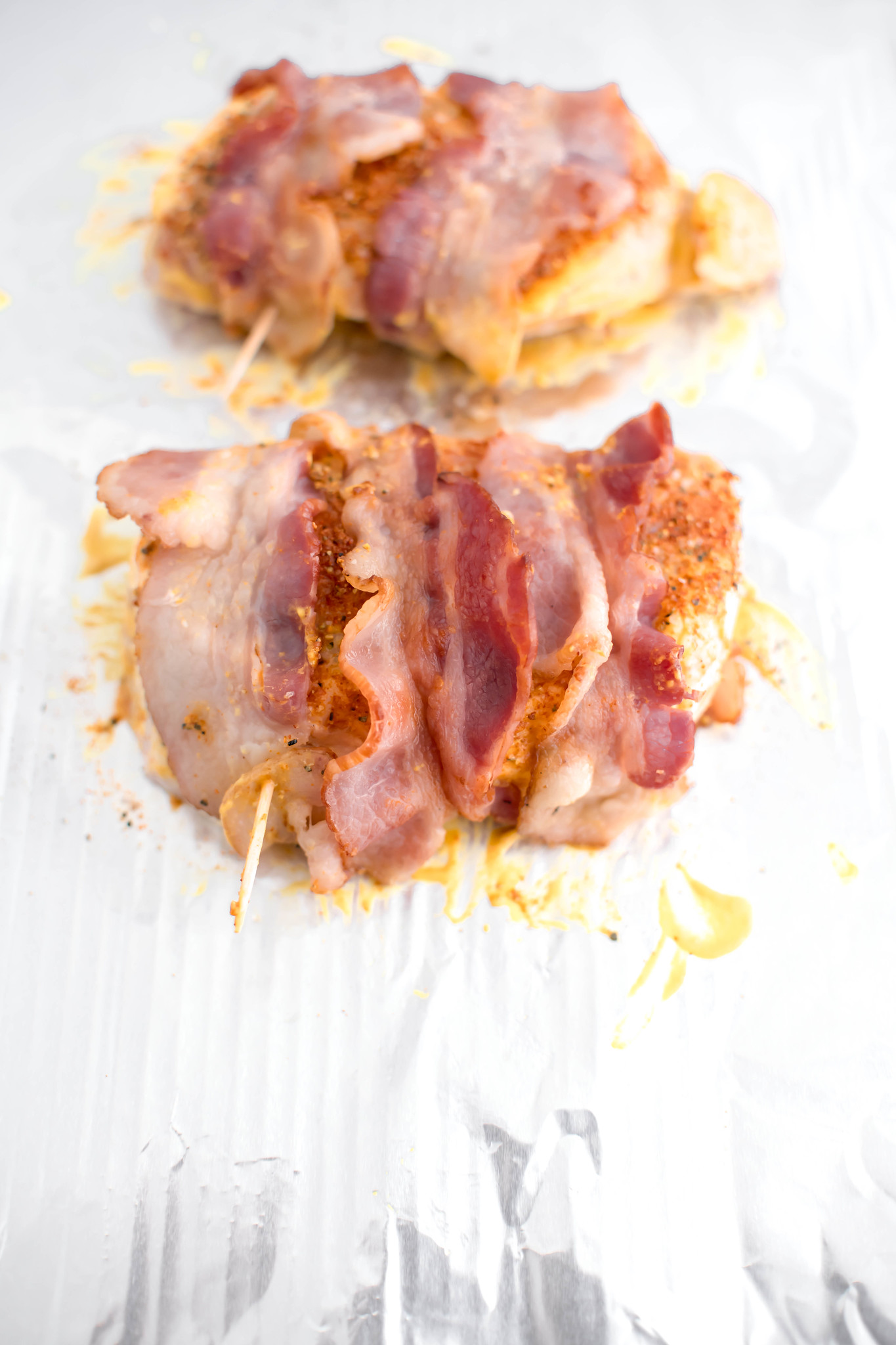Pork chops rubbed in mustard and spices and wrapped with bacon on a baking sheet.
