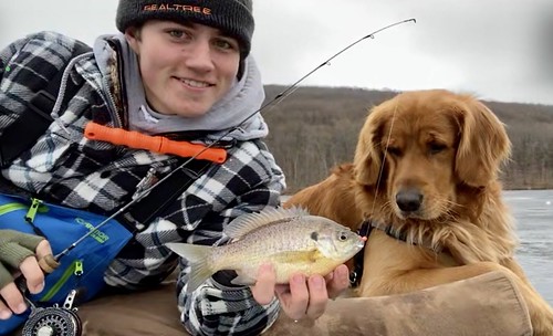 Photo of young man and dog holding a fish next to some iced-over water