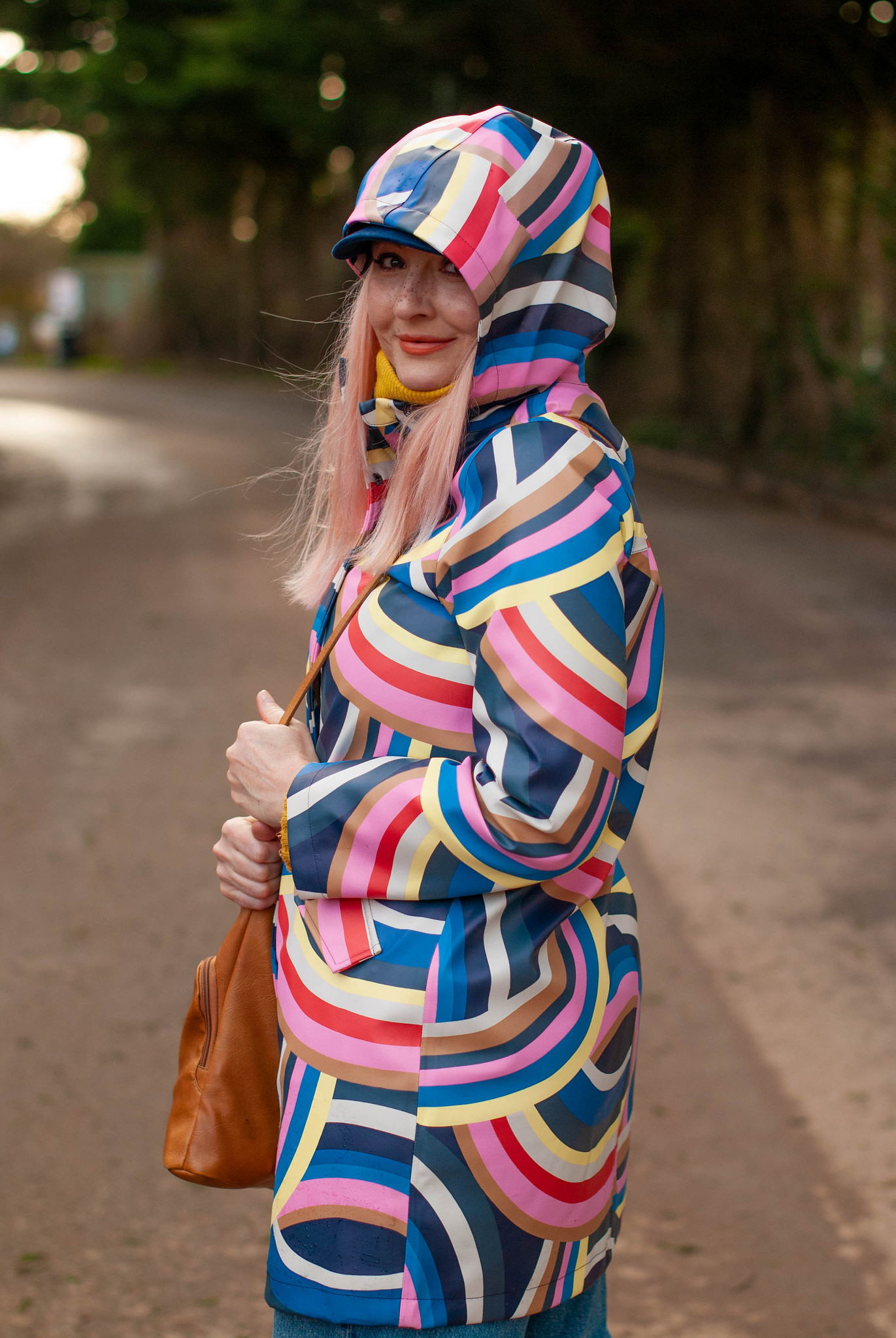 The Catheriniest Raincoat Ever: Catherine Summers AKA Not Dressed As Lamb wearing a bold rainbow raincoat, mom jeans, navy Chelsea boots, mustard sweater and navy baker boy hat | Style Over 50