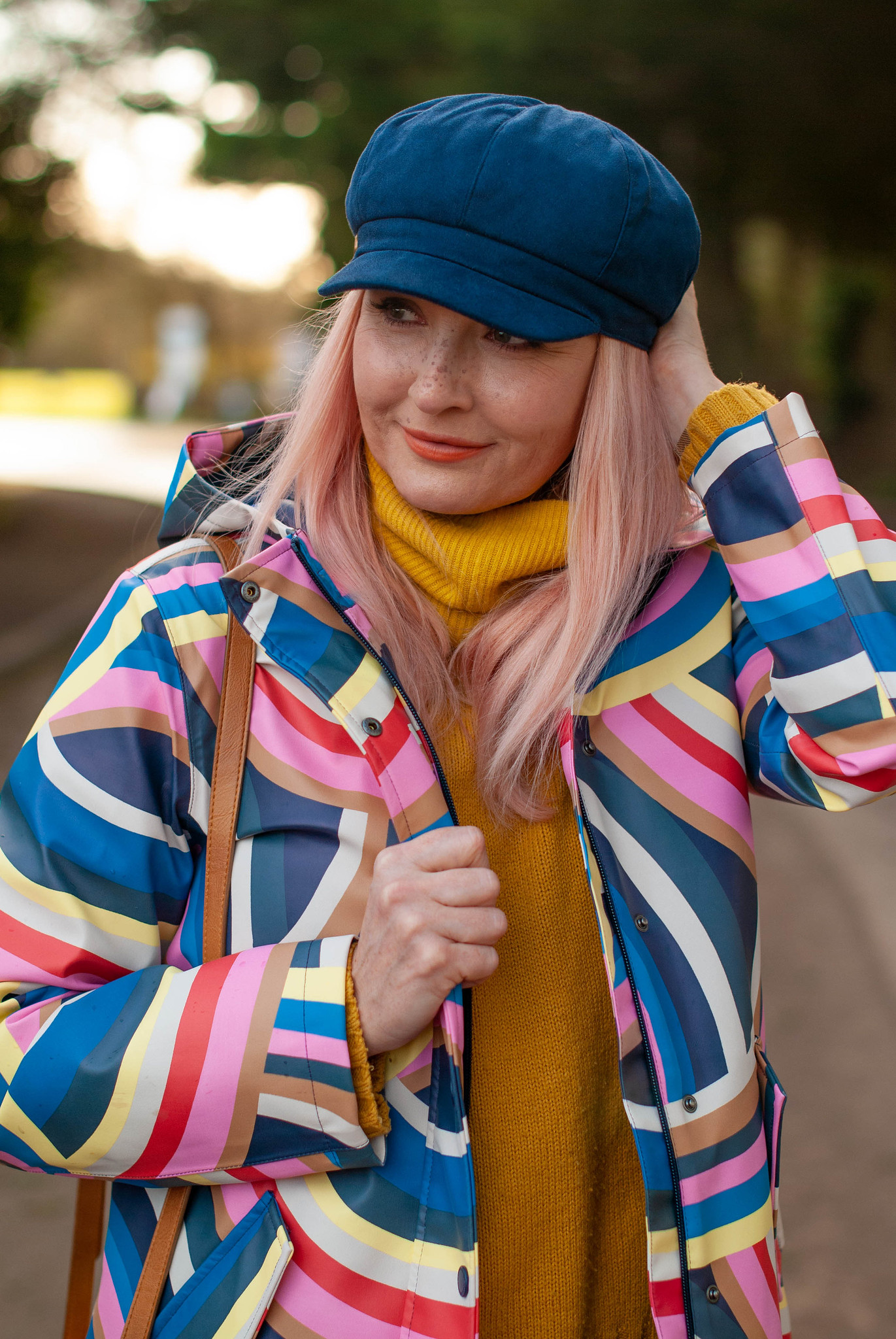 The Catheriniest Raincoat Ever: Catherine Summers AKA Not Dressed As Lamb wearing a bold rainbow raincoat, mom jeans, navy Chelsea boots, mustard sweater and navy baker boy hat | Style Over 50