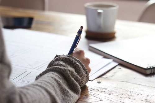 A person sits at a table and writes on a paper with pen - Como Empezar a Planear para el Colegio