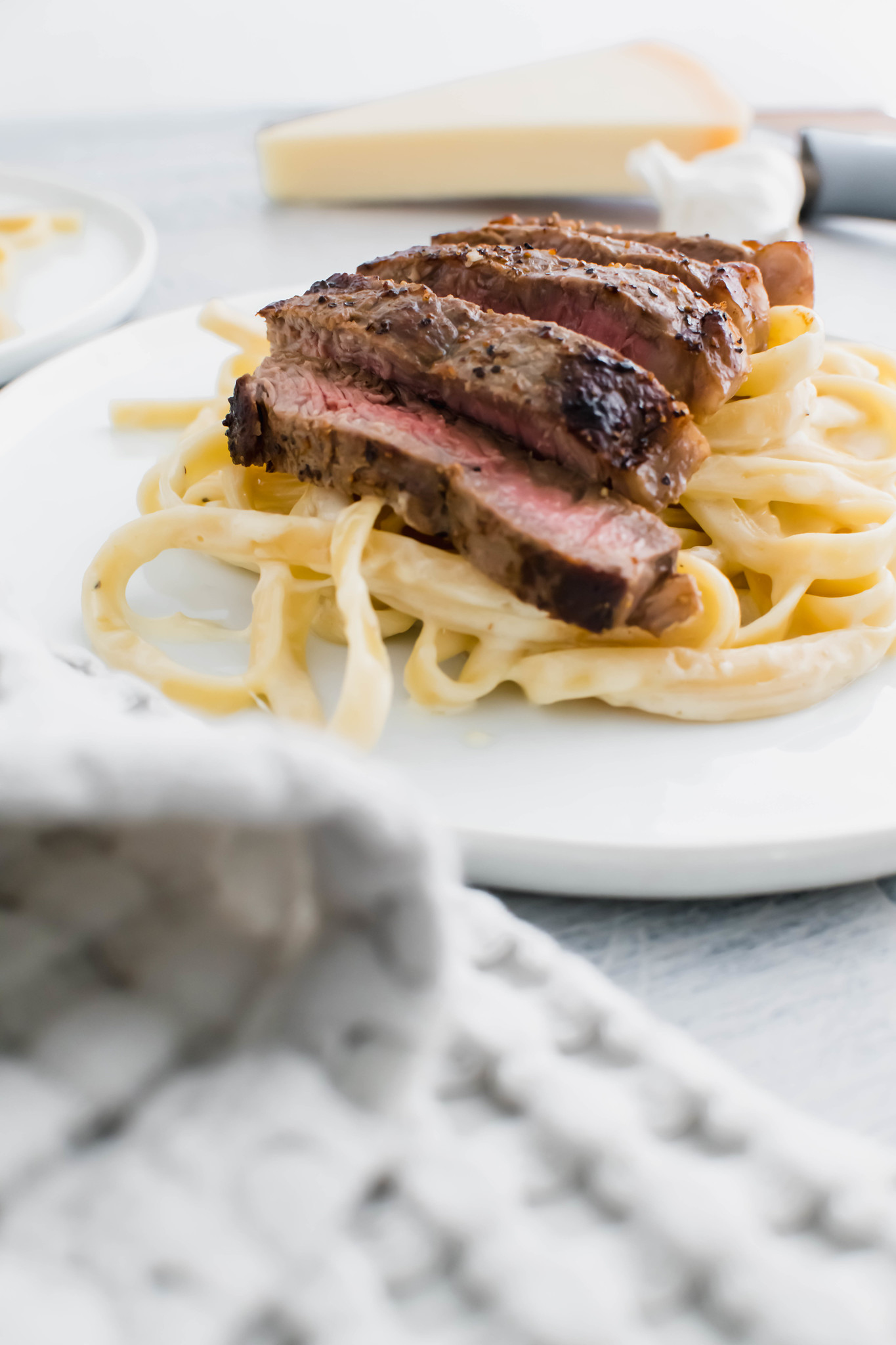 White round plate with fettucine alfredo topped with sliced steak.