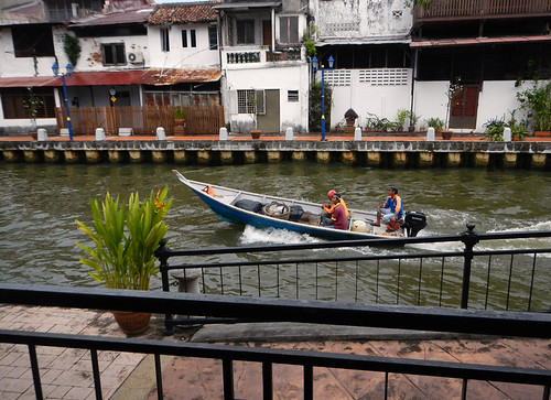 Boat racing down a canal past a row of houses in Melaka, Malaysia