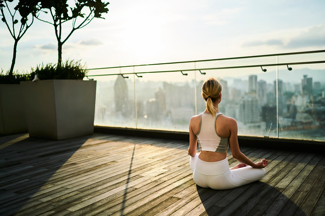 Back view of slim girl in active wear sitting in lotus pose recreating on spiritual practice and keeping healthy lifestyle, caucasian female relaxing on yoga practice feeling calm on rooftop