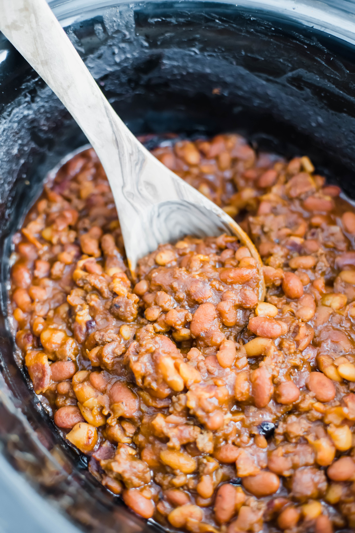 Wooden ladle in slow cooker filled with cowboy baked beans.