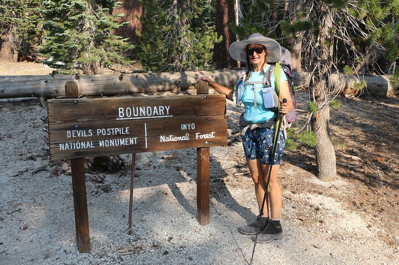 Vicki standing at the sign showing the northern boundary of Devils Postpile NM and the Inyo NF on the JMT