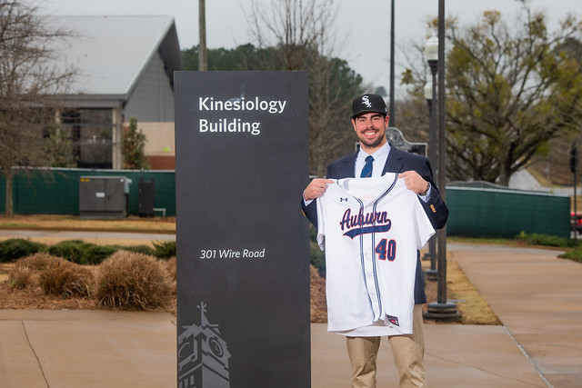 Bo Plagge holding up an Auburn club baseball jersey in front of the School of Kinesiology.