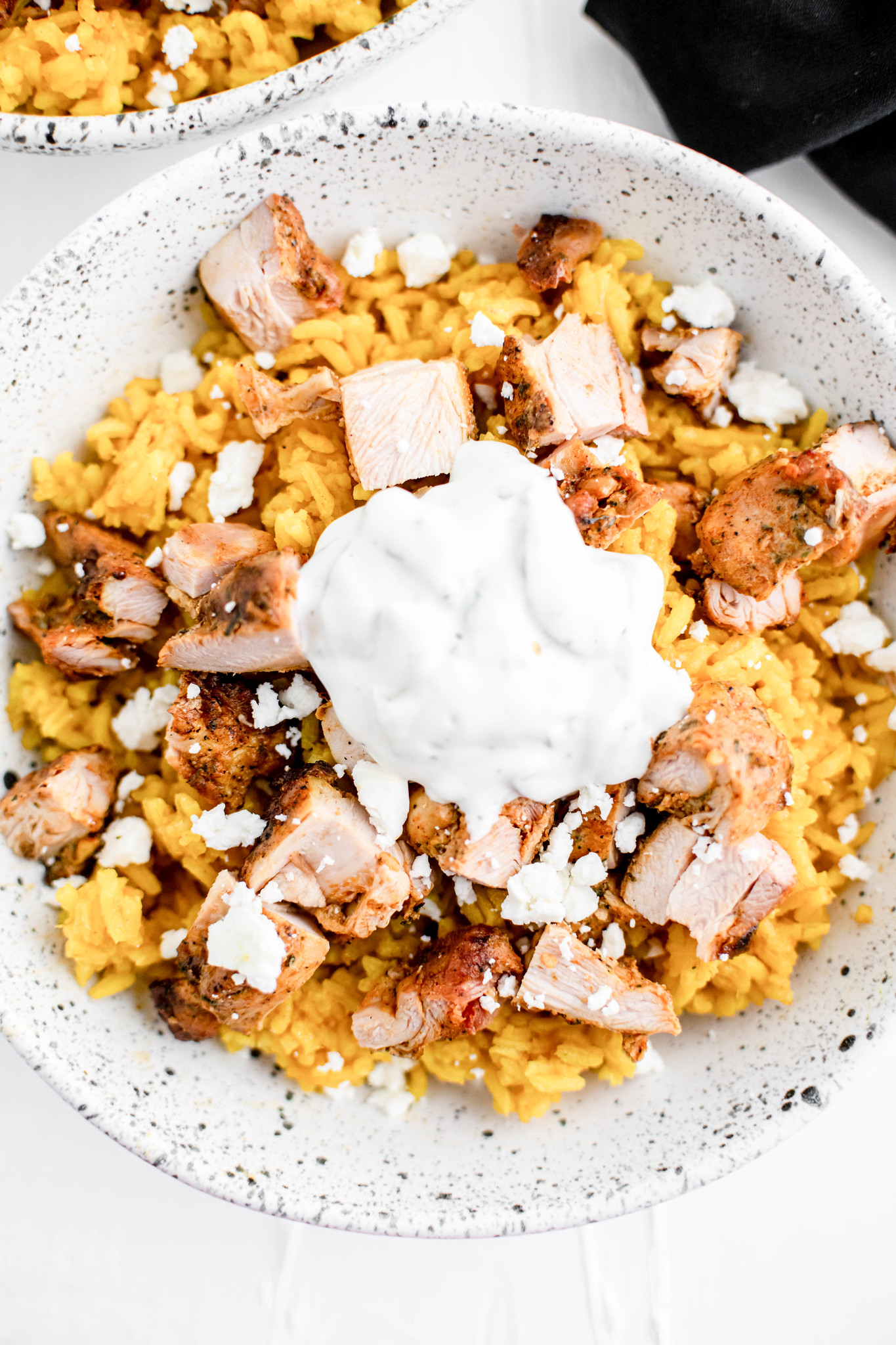 Bowl filled with golden tumeric rice that is topped with diced shawarma chicken, crumbled feta cheese and a dollop of tzatziki.