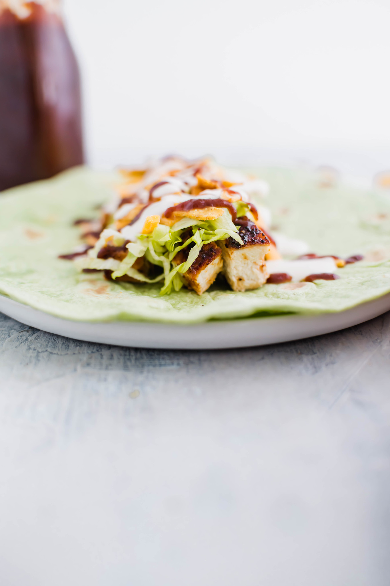Spinach tortilla on a plate with barbecue chicken, lettuce, cheese, tortilla strips, barbecue sauce and ranch on top.