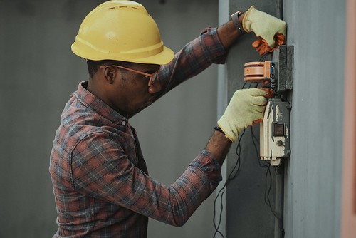 A man with a hard hat and glasses fixes an electrical box - Gap Years: Pros, Cons, & How to Make them Effective