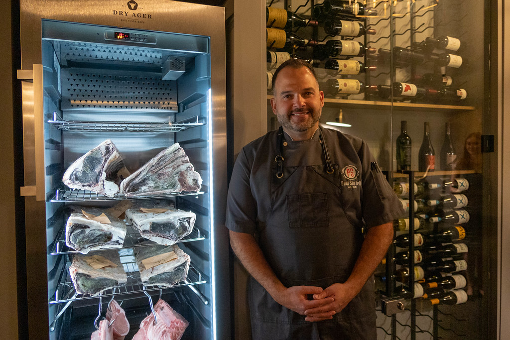 Paul Shufelt in front of a wine rack and a refrigerator full of meat