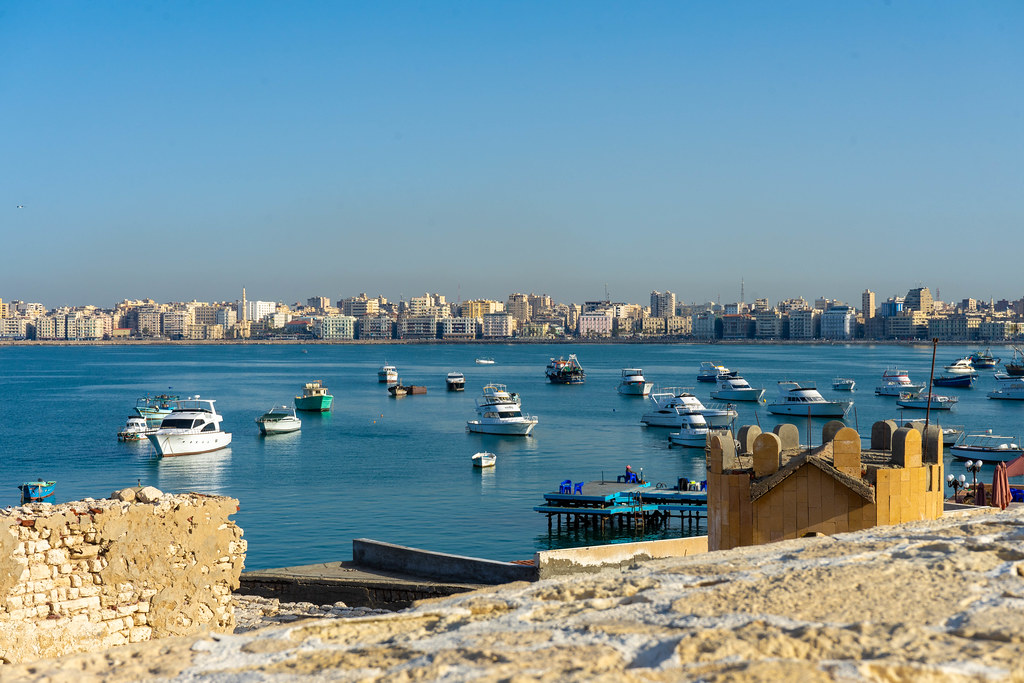 Alexandria seen from the walls of the citadel, over the sea. There are many boats anchored between the citadel and the shore. The weather is beautiful, with no clouds in the sky
