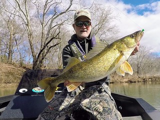Photo of a man in small boat holding a large walleye fish