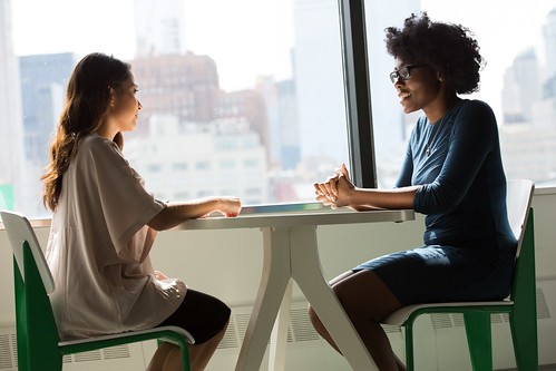 One woman intently interviewing another, their shared table bathed in natural light from a large window overlooking the bustling cityscape. - The Dos & Don'ts of Asking for Job References