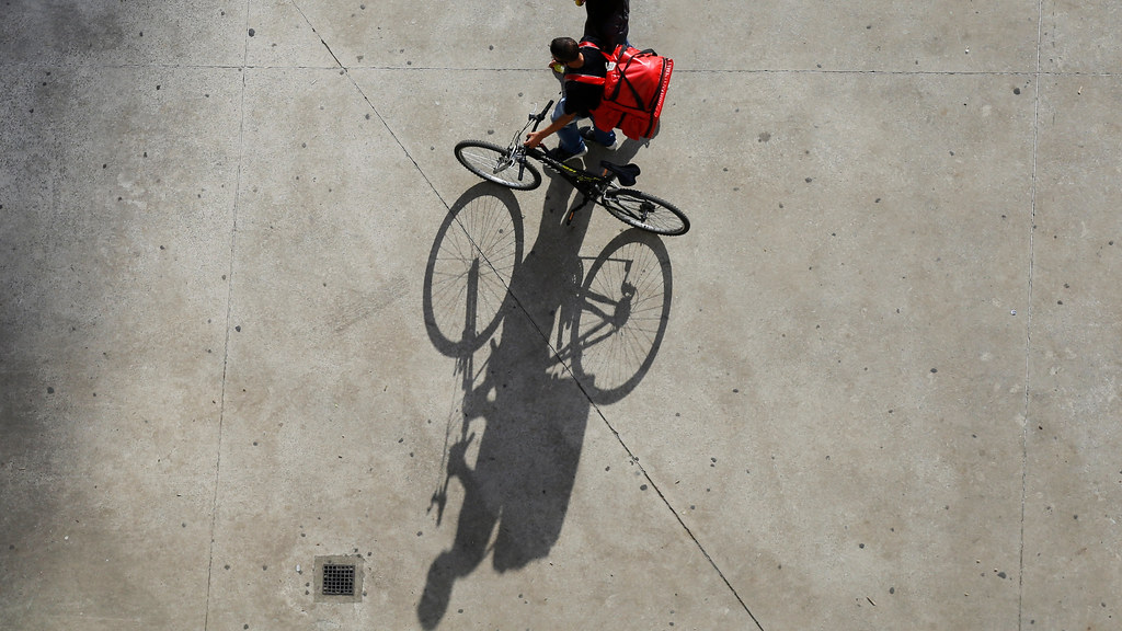 Image of young man cycling bike in Brazil, carrying a delivery, with shadow.